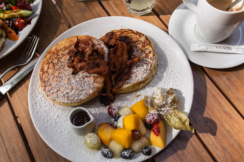 Pancakes mit Bacon und Ahornsirup im Café von der Motte in Hamburg, Ottensen. Dazu gibt es einen Obstsalat