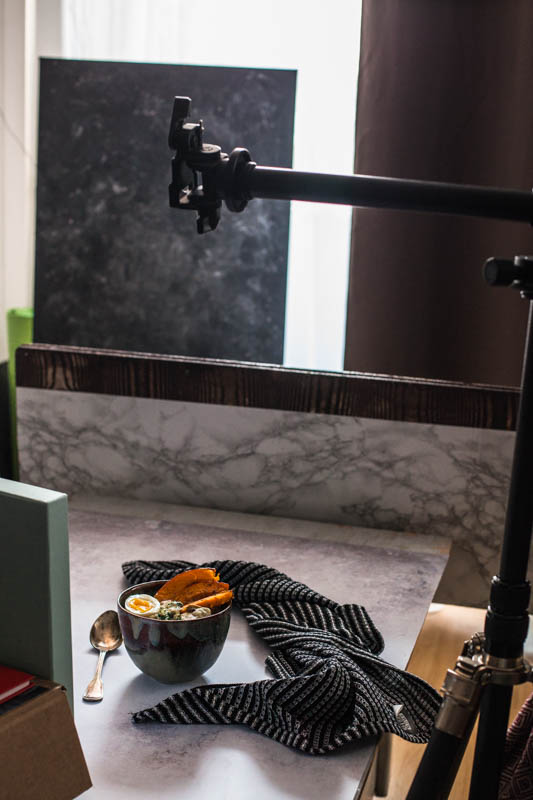 Behind the scenes food photography shot showing a bowl placed on a photo backdrop and backlight from a window that is partly obscurred by a curtain 