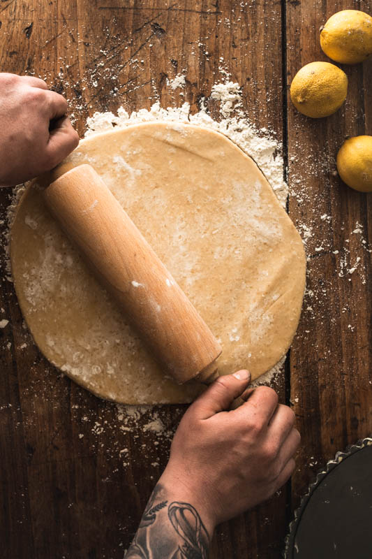 Masculine hands rolling out a dough on a rustic wooden surface