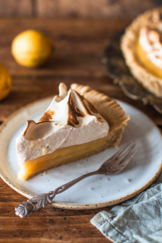 One piece of vegan lemon meringue pie placed on a handmade white plate. The overall feeling is very rustic and cozy.
