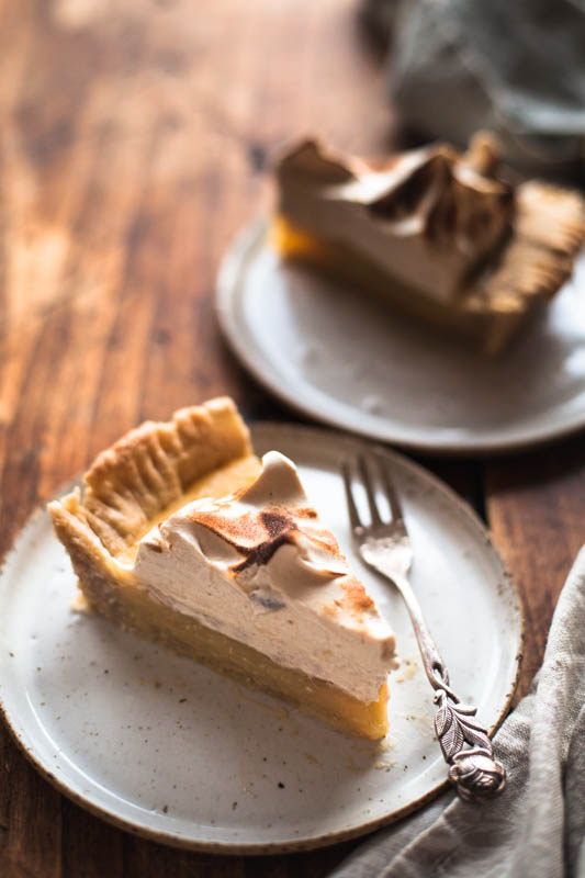 One piece of vegan lemon meringue pie placed on a handmade white plate. The overall feeling is very rustic and cozy.