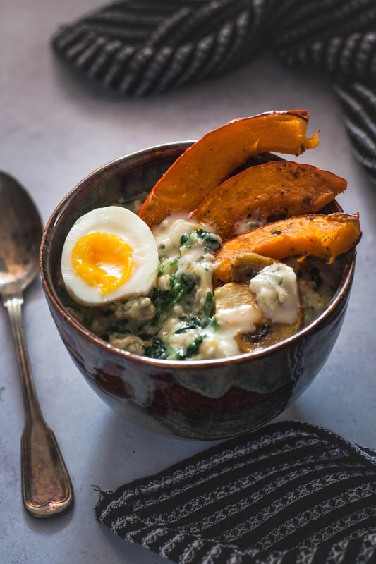 Eine Schüssel deftiges Porridge mit Kürbis, Spinat und Ei bei Tageslicht fotografiert. 