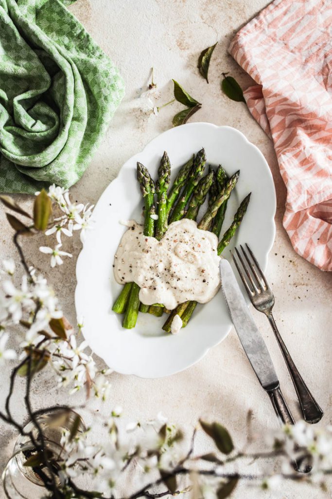 Eine frühlingshafte Food Fotografie mit grünem Spargel. Es wird mit Blumen und Schärfentiefe gespielt.